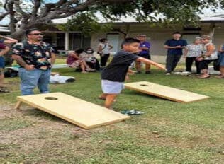 Daryl of WHM aims and tosses the bean bag in hopes of getting it in the cornhole as father, Mackey Noguchi looks on.